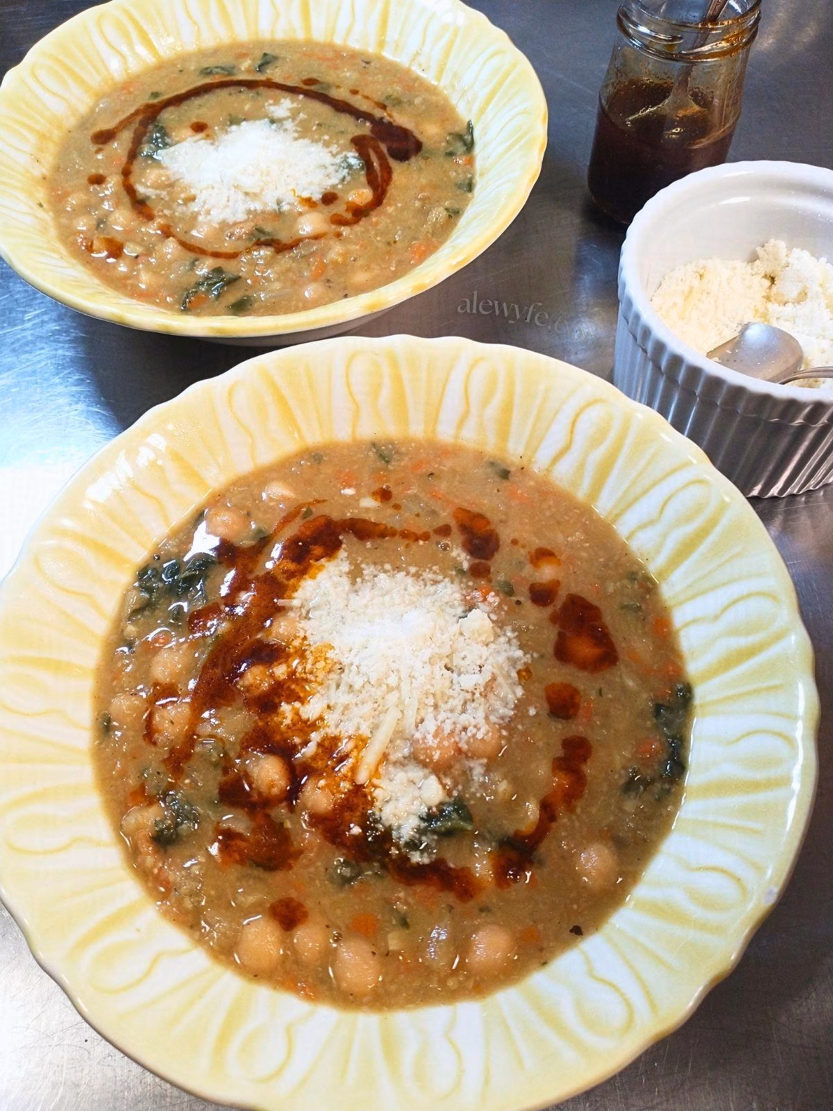 two bowls of chickpea chard stew, garnished with grated cheese and paprika oil.
