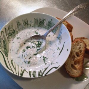 a small bowl of dill horseradish crema, topped with sprinkles of fresh dill, with a plate of baguette croutons.