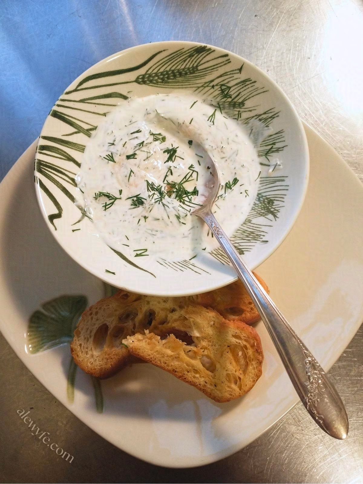 horseradish dill crema dip in a bowl, with a silver spoon and toasted bread crackers.