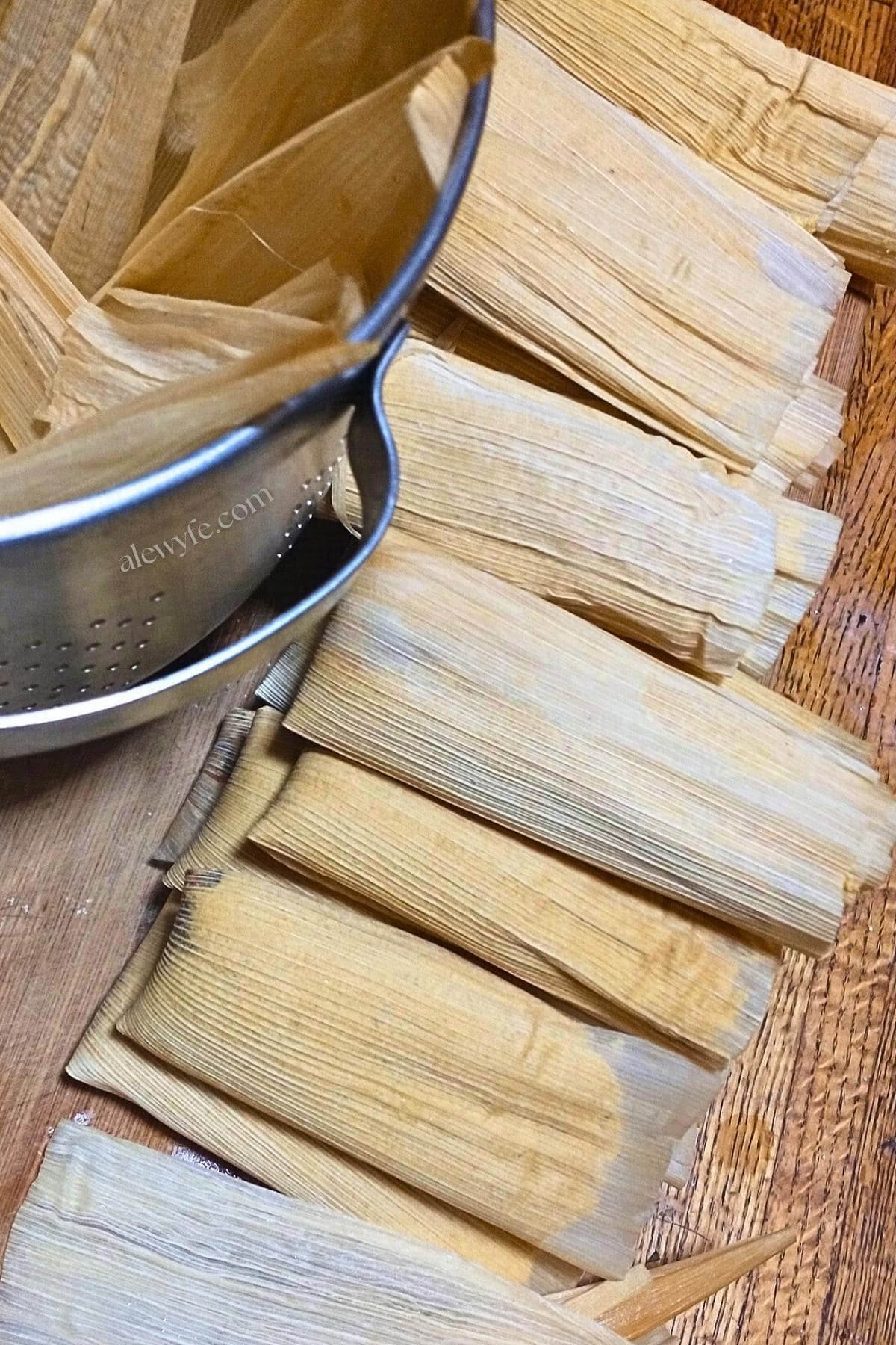 a row of rolled and filled pumpkin mincemeat tamales ready to be stacked into the metal steamer lined with corn husks.