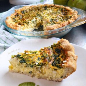 a slice of spinach, feta and artichoke quiche on a plate with the quiche in the background.