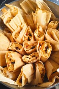 a stainless colander full of pumpkin tamales filled with mincemeat ready to steam and eat.