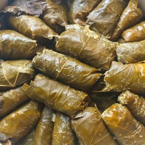 a pan of stuffed grape leaves, stuffed with rice, nuts, dried fruit, herbs, and spices. The rolled dolma are stacked in the pan and ready to serve.