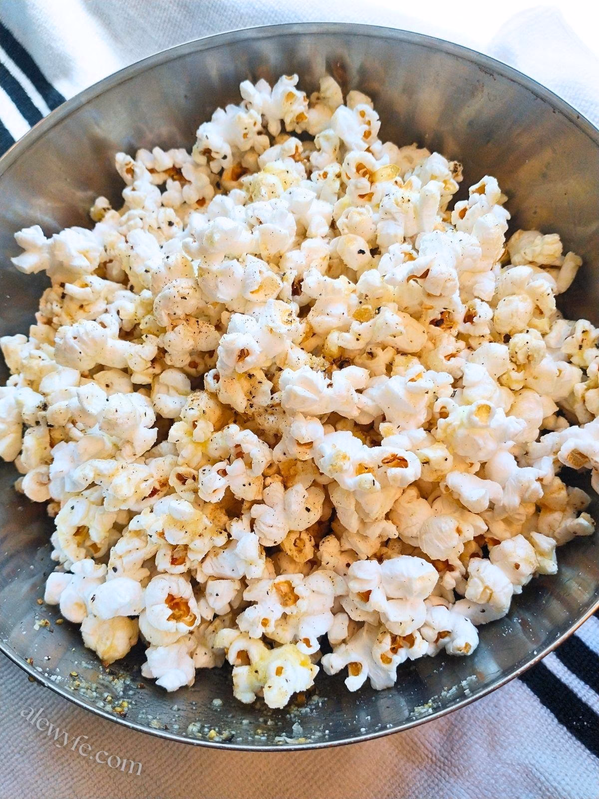 top-down photo of a bowl of popcorn with black pepper, sea salt, grated parmesan, butter, and truffle oil.