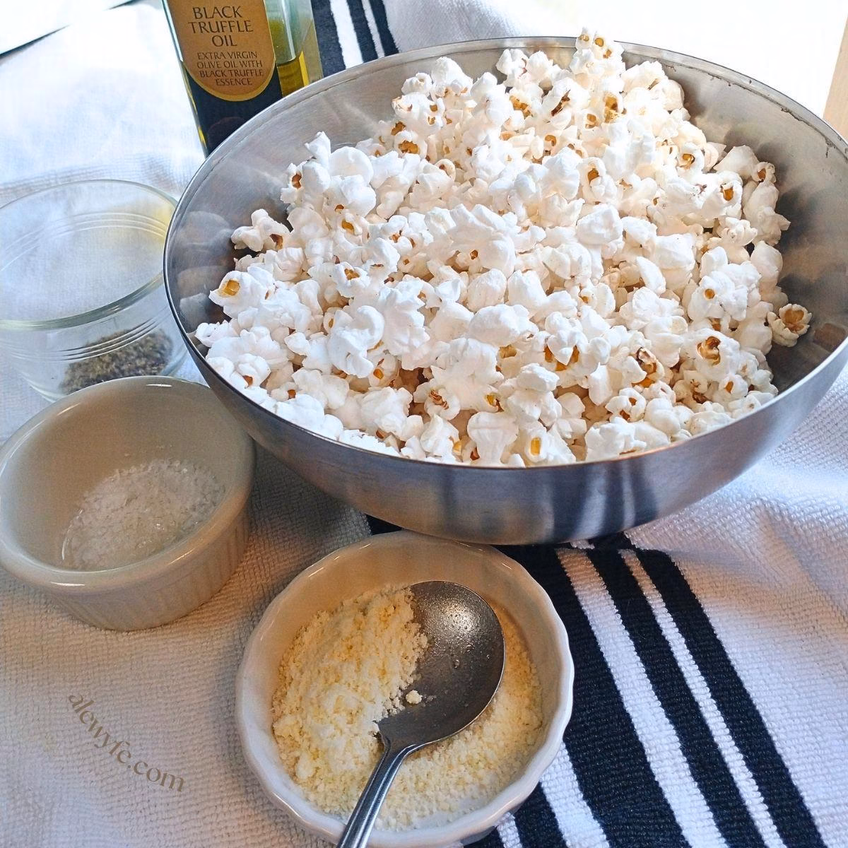 a bowl of popcorn, surrounded by small ramekins of Parmesan cheese, flaky sea salt, black pepper, and a bottle of black truffle oil.