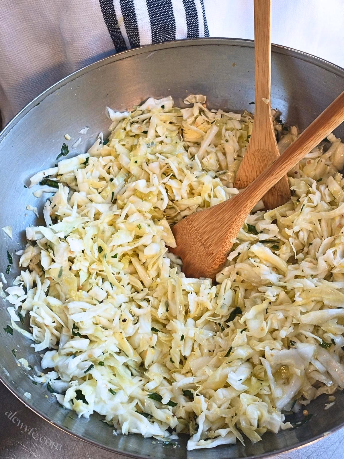 a bowl of cabbage salad with lemon garlic vinaigrette with bamboo tongs.
