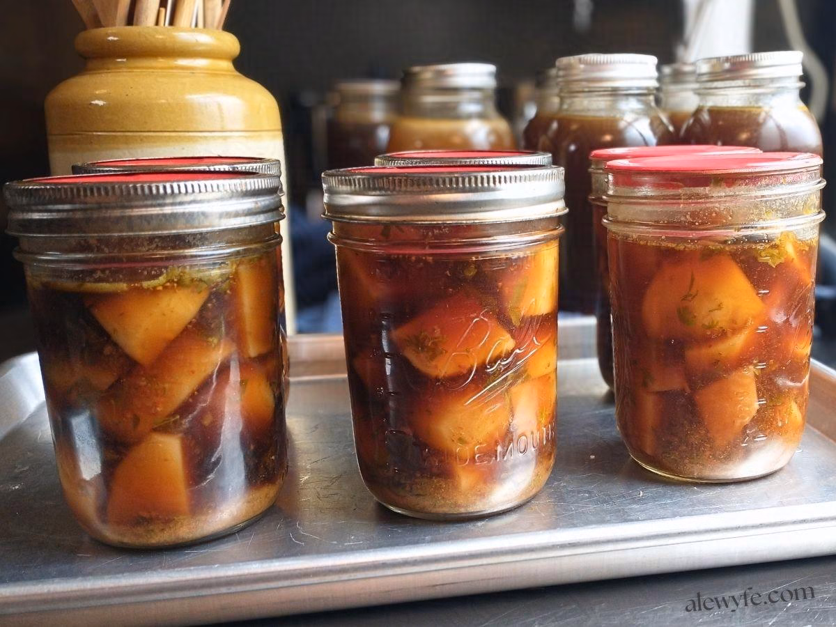 jars of canned chipotle potatoes cooling on a tray with jars of stock in the background.