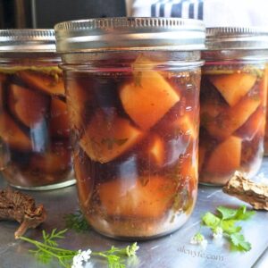 pint jars filled with seasoned diced potatoes canned with chipotle pepper and cilantro. Dried chipotle chiles and fresh cilantro sprigs are in the foreground.