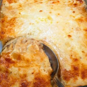 close-up of a shepherd's pie casserole, with a large silver serving spoon breaking through the cheesy potato topping to scoop out a serving of the dish.