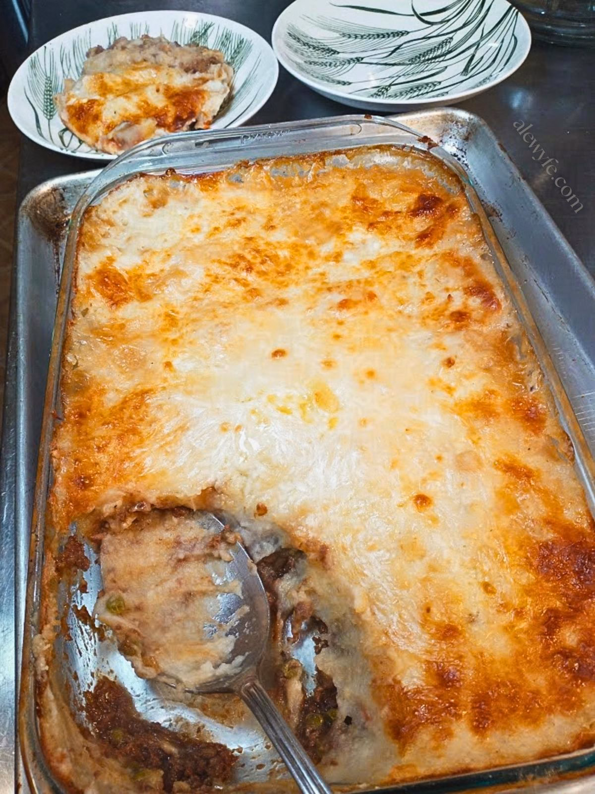 a baked hunter's cottage pie with one large serving plated, with a serving spoon in the baking dish.