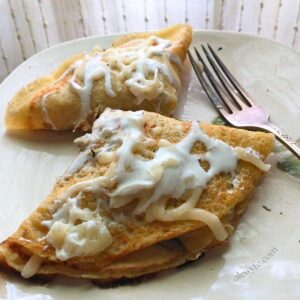 folded crepes on a plate, filled with spinach & artichoke cheese filling, and topped with melted cheese and a drizzle of crema.