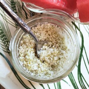 close-up of a jar of homemade tangy lime salt, with a tiny spoon with a faux-wood print on the handle.