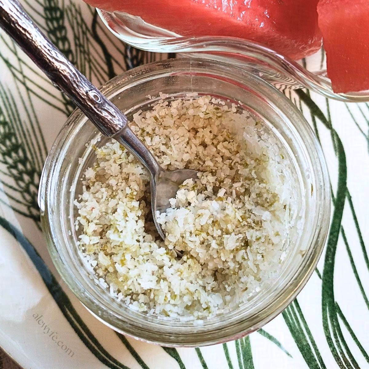close-up of a jar of homemade tangy lime salt, with a tiny spoon with a faux-wood print on the handle.