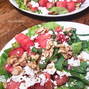 close-up of a plated watermelon salad with fresh greens, feta, and toasted walnuts.
