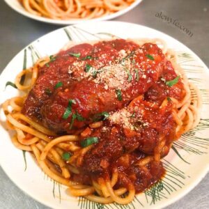 a close-up photo of a plate of homemade hot Italian venison sausage links braised in tomato ragu on a bed of bucatini noodles.