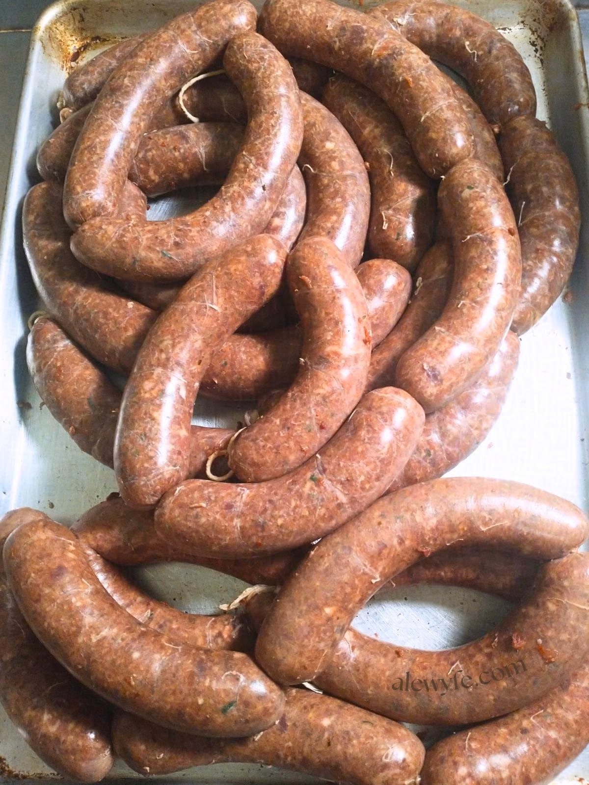 a metal sheet tray piled up with freshly stuffed hot Italian sausages.